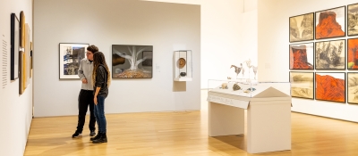 Two college-age students stand in a museum gallery installed with works by both American and Native American artists. Some works are contemporary and some are not. 