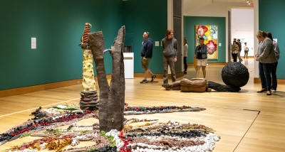 An instillation image of "Immersive Worlds: Real and Imagined" on view now in Lathrop, Jaffe, and Hall Galleries. In this photo people stand in a green room surrounded by colorful art. They are admiring the art.