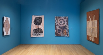 An installation of Indigenous Australian bark paintings hung on a teal wall.