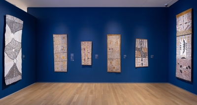 Indigenous Australian bark paintings hanging in a museum gallery with dark blue walls.