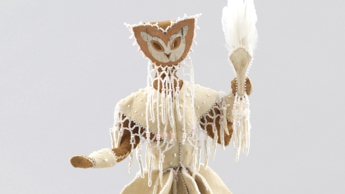 A figure made of tanned hide, wearing a mask, and holding a fan with feathers.