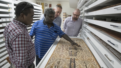Indigenous Australian artists discuss their bark paintings with museum curators in art storage.