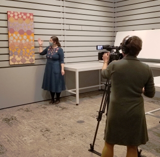 A museum educator is being filmed in a classroom for a virtual college course. She is discussing an Aboriginal Australian painting.