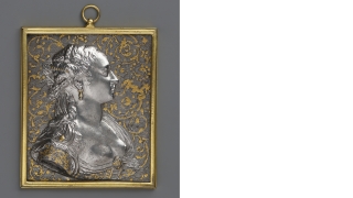 A silver and gold square plaquette of a woman in profile.