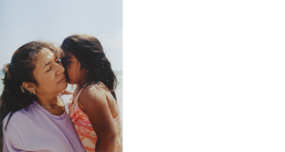 A woman embraces a young girl. The image is zoomed in, so their faces and upper torsos are visible. 