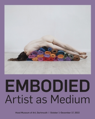 A cover of an exhibition brochure that features of photograph of a female nude that is facing away from the viewer and reclines uncomfortably on a stack of colorful yoga mats. The brochure's accent color is purple.