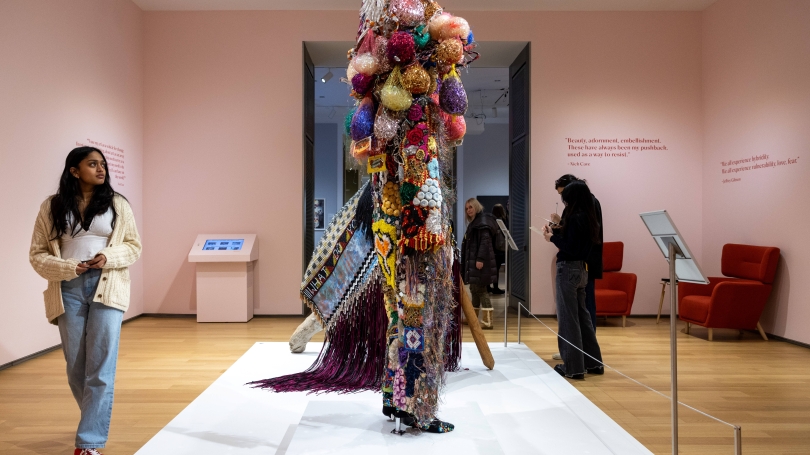 Three women walk around a brightly colored sculpture in the middle of a pink room.