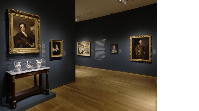 A museum gallery with dark blue-gray walls, installed with American art from the colonial era to present day.