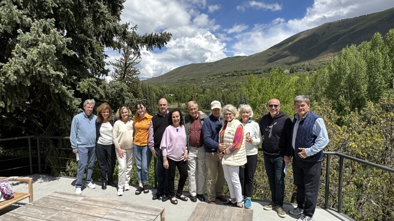 John Stomberg (middle) is pictured in a black sweater vest. He is photographed on a porch surrounded by members of the Directors Circle. The group is being photographed in Aspen, Colorado with a green mountain in the back.