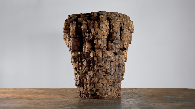 A large cedar toned pleated bowl with sides that are reminiscent of a cliff or bolder sits on display. 