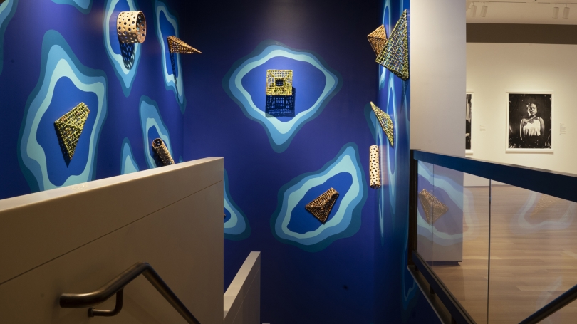An installation shot of two shows. On the right, CIPX, a show of black and white photography. On the left, an installation of wall-mounted ceramic sculptures on a cerulean background, meant to look like water.