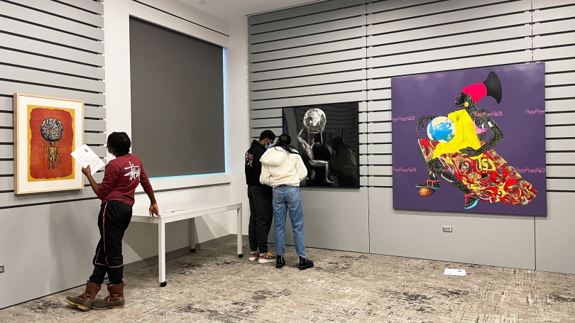 Three college-aged students look at work by African American artists in a smart classroom.