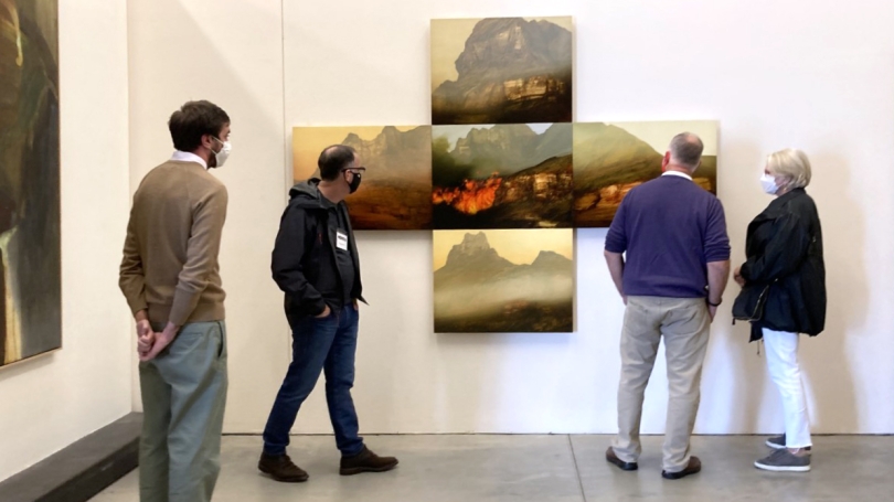 Adults look at contemporary landscapes in a gallery with white walls.