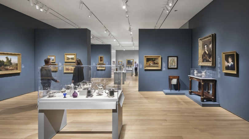 American art from the Hood's permanent collection in the new second-floor galleries. The walls are blue and there is a large display case in the center of the gallery with ceramics inside it.