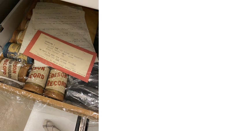 Plastic-wrapped Edison cylinders with a typed note on top. Note reads: "WARNING! There are TWO (2) kinds of records: Black (soft-wax) slow Blue (hard): LP Be sure to use the proper needle. There are TWO KINDS. Failure to do so will wreck the record.
