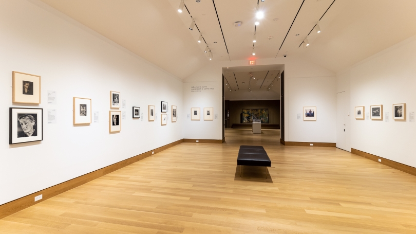 A museum gallery and installation of portrait photography. The portraits are mostly black and white and the gallery walls are white.