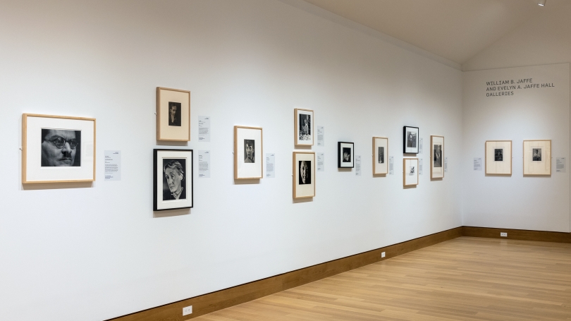 A museum gallery and installation of portrait photography. The portraits are mostly black and white and the gallery walls are white.