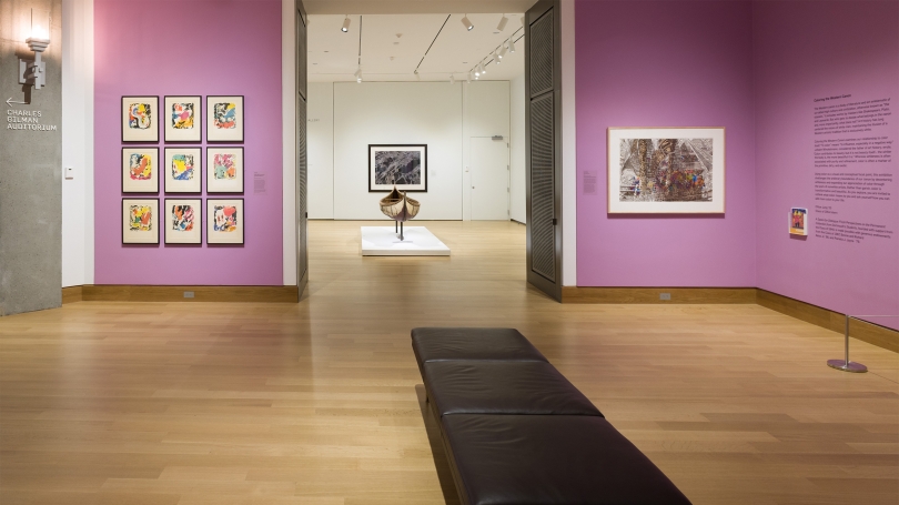 A museum gallery with lilac purple walls and colorful works of art hanging on the walls. 
