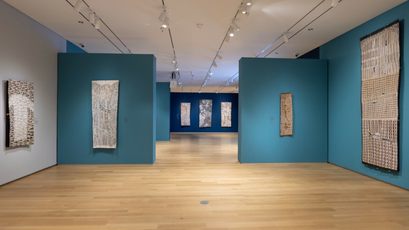 A museum gallery with teal walls installed with large-scale Indigenous Australian bark paintings.