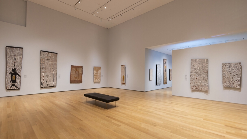 A museum gallery with white walls is installed with large-scale Indigenous Australian bark paintings.