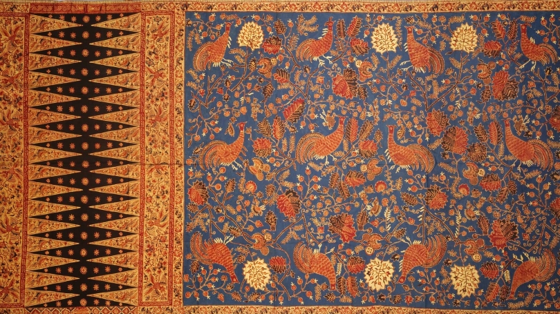 Rectangular orange-gold textile with a black diamond pattern on the left and red-orange roosters with a blue background on the right.