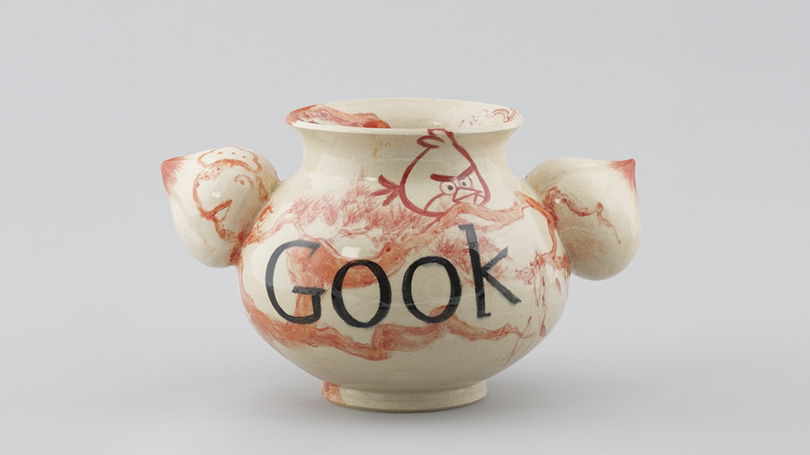 A white stone wear ceramic vase with red and black underglazes adorning it. The vase has the words "Gook" in black lettering as well as red depictions of "Angry Birds."