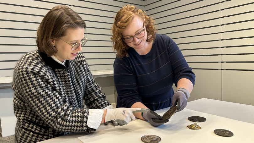Two women study coins and medals made of different kinds of metals from 1400–1750s. 