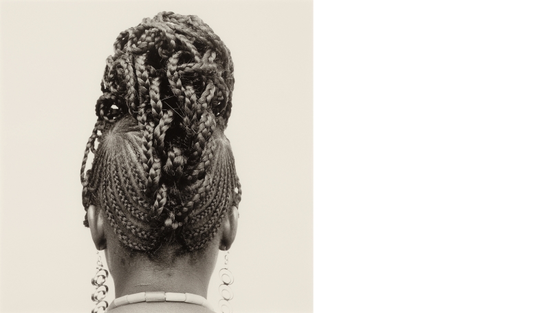 Black-and-white photograph of the back of a woman's head. Her hair is braided and the braids shaped into a large, intricate bun at the top of her head.