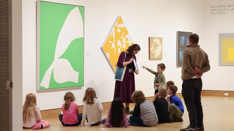A group of students listen to a teacher discuss the art on the walls