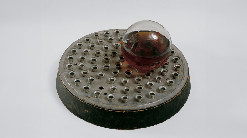 a glass ball filled with whiskey sits atop a circular metal base with raised holes