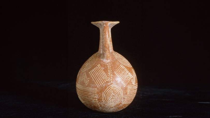 side view of an orange jug with white engravings on it.