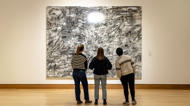 Dartmouth students view a large-scale painting in the galleries.