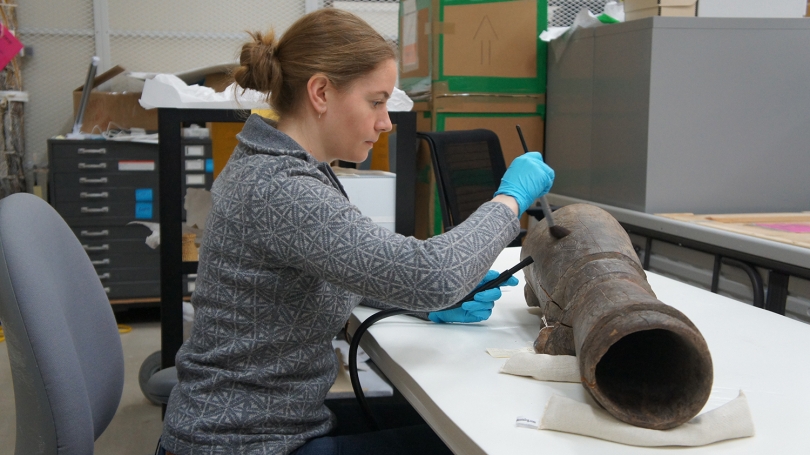 Annika Cilke, assistant conservator of objects and textiles, Williamstown Art Conservation Center, cleans the surface of a Papua New Guinean hand drum, using a soft-bristle brush to guide dust into a small, low-suction filtered vacuum nozzle.